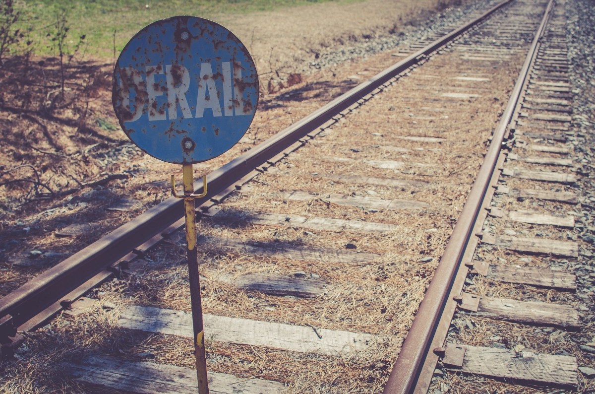 A rusted sign reading "Derail" by railroad tracks